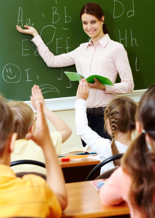 Explanation of teacher Portrait of smart teacher pointing at blackboard and looking at schoolkids in classroom